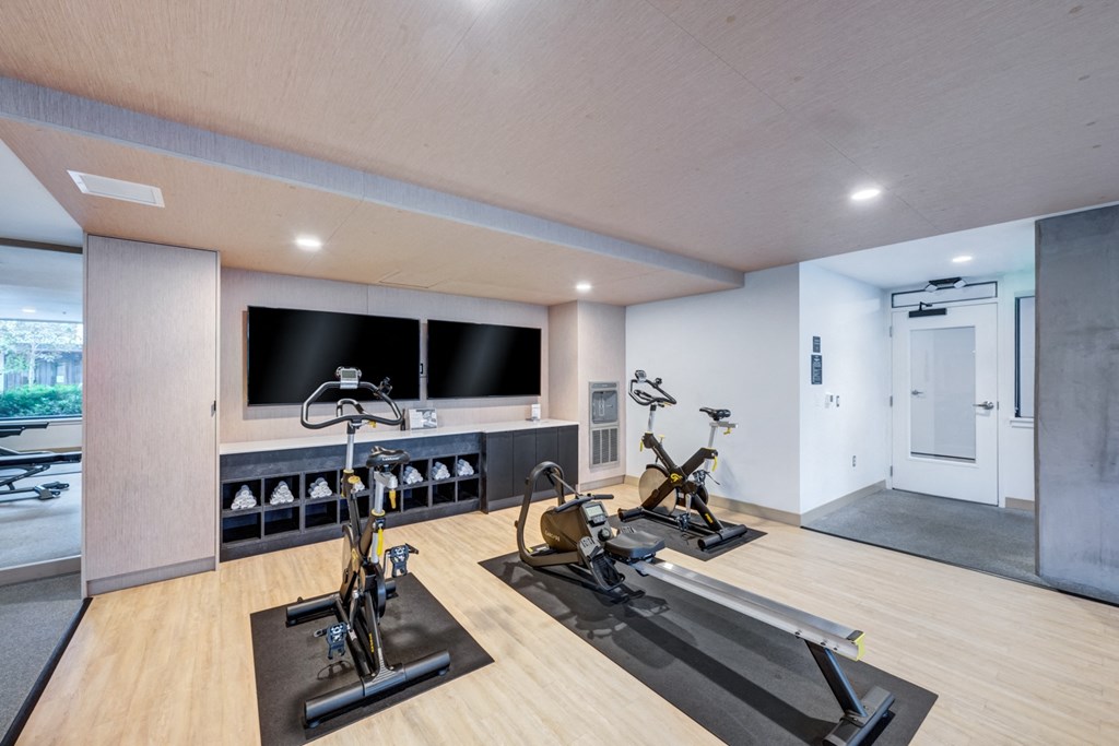 A room with a wooden floor and a wall-mounted television displaying a black screen.